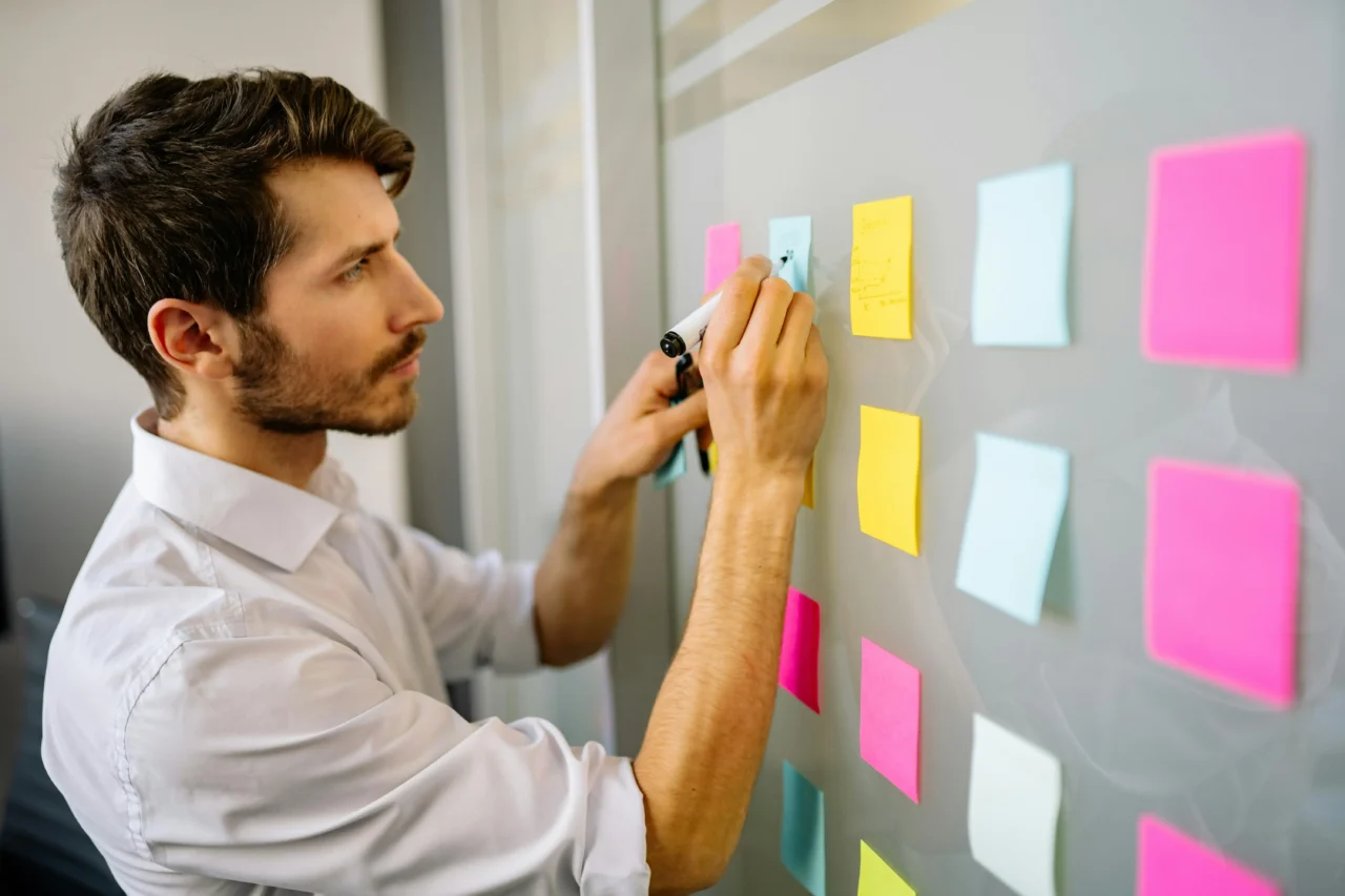 Man writing on sticky notes attached to wall in a meeting room, representing someone not using AI in the workplace.