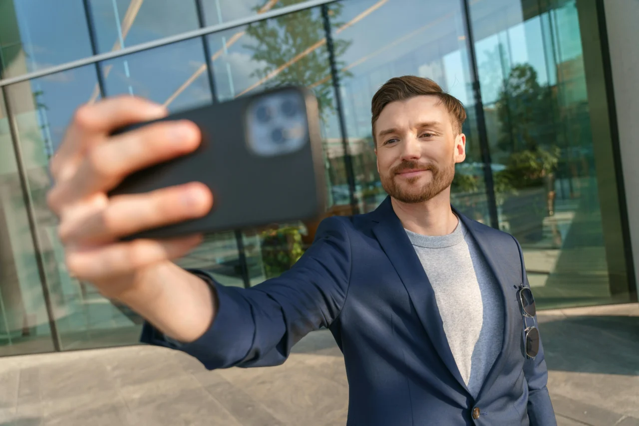 Employee advocacy example: man in suit taking selfie in front of modern office building